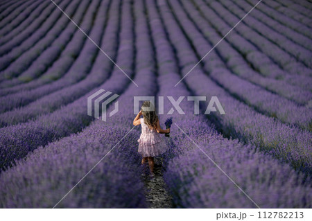 Lavender field girl. Back view happy girl in pink dress with flowing hair runs through a lilac field of lavender. Aromatherapy travel 112782213