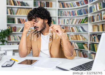Tired muslim man taking of glasses and rubbing eyes with closed eyes while working by laptop. Stressed retired manager waiting for break while having vision struggles due to long screen time. 112782745