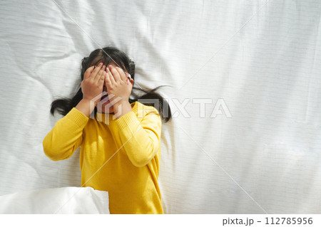 Sad child covered his face with his hands while lying on the bed at home.  112785956