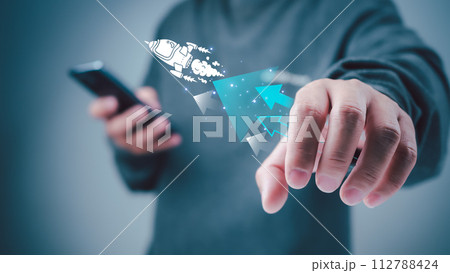 Start up business concept to success, Man holding smartphone and white rocket icon is launch and soar flying out from screen with network digital technology, Finance business growth concept. 112788424