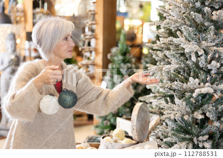 Mature woman purchasing christmas toys and decorations at christmas fair shop Mature woman purchasing christmas toys and decorations at christmas fair shop 112788531