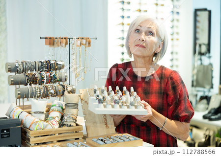 Cheerful elderly woman choosing rings from display with costume jewelry in boutique Cheerful elderly woman choosing rings from display with costume jewelry in boutique 112788566