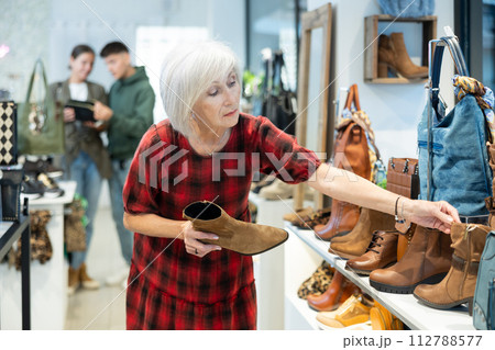 Elderly woman chooses ankle boots in store 112788577