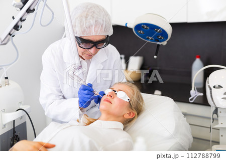 Cosmetologist using laser to resurface skin of young woman's face Cosmetologist using laser to resurface skin of young woman's face 112788799
