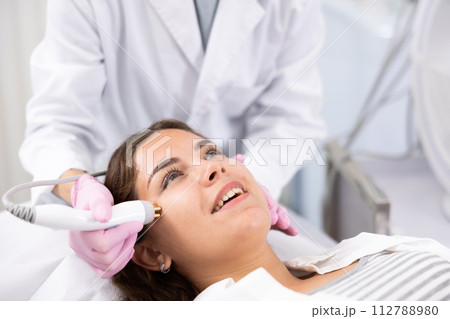 Mature female dermatologist performing cosmetology procedure for young woman, RF lifting and vacuum massage for facial skin therapy in clinic Mature female dermatologist performing cosmetology procedure for young woman, RF lifting and vacuum massage for facial skin therapy in clinic 112788980