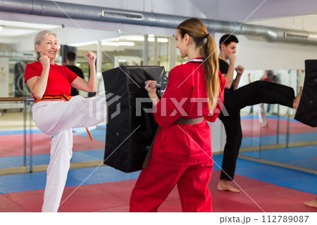 Aged woman kicking shield in martial arts training at gym 112789087