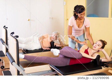 Young woman practicing pilates on reformer with female trainer Young woman practicing pilates on reformer with female trainer 112789096