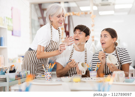 Cheerful older woman with young adult children painting pottery in family workshop Cheerful older woman with young adult children painting pottery in family workshop 112789097