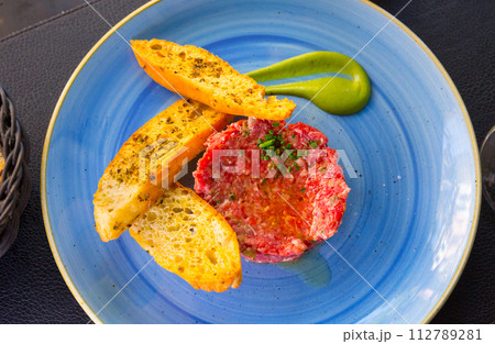 Close up of tasty veal steak tartar served at blue plate with toasts Close up of tasty veal steak tartar served at blue plate with toasts 112789281