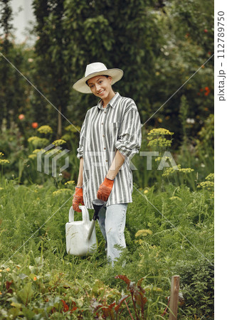 Gardening in summer. Woman watering flowers with a watering can. Girl wearing a hat. Gardening in summer. Woman watering flowers with a watering can. Girl wearing a hat. 112789750
