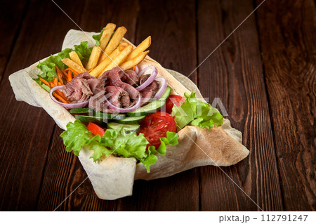 Meat salad with beef and fresh vegetables and lettuce in a plate-baked pita bread. Copy space, wooden background. 112791247