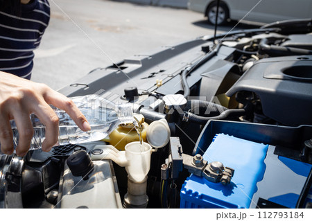 Closeup,Hand of woman pouring clean water into the windshield washer fluid tank of a car,filling the windshield washer fluid with plain water,check liquid level in engine room,car maintenance concept Closeup,Hand of woman pouring clean water into the windshield washer fluid tank of a car,filling the windshield washer fluid with plain water,check liquid level in engine room,car maintenance concept 112793184