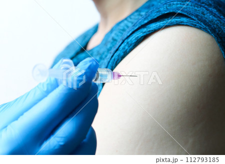 A doctor's hand holds a syringe and the doctor is about to inject a vaccine into the arm of a man at the hospital. health and medical concepts A doctor's hand holds a syringe and the doctor is about to inject a vaccine into the arm of a man at the hospital. health and medical concepts 112793185