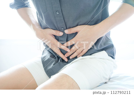 Young man uses his hands to hold his stomach and has a severe stomachache. Young man uses his hands to hold his stomach and has a severe stomachache. 112793211
