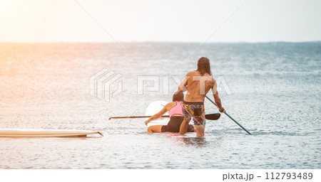 Sea woman and man on sup. Silhouette of happy young woman and man, surfing on SUP board, confident paddling through water surface. Idyllic sunset. Active lifestyle at sea or river. 112793489