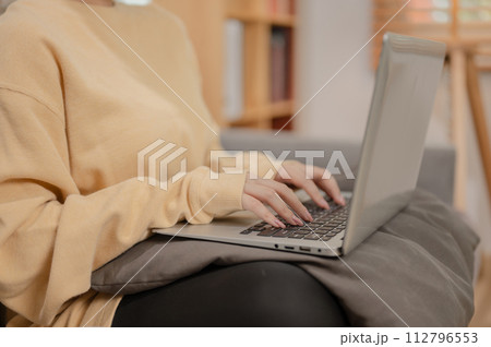 A woman in comfy clothes working on her laptop computer on the sofa in the living room. 112796553