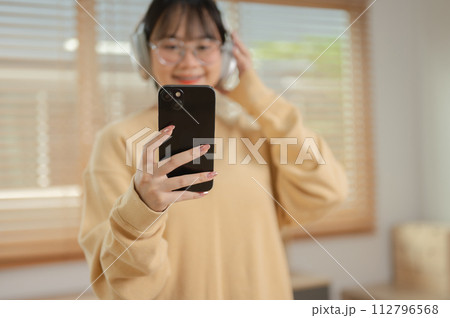 A cute Asian woman is listening to music on her headphones and using her phone in the living room. A cute Asian woman is listening to music on her headphones and using her phone in the living room. 112796568