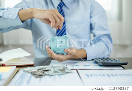 Hand putting coin into piggy bank. Saving money with coins steps into a successful growing business, and saves it for retirement. Retirement Savings concept Hand putting coin into piggy bank. Saving money with coins steps into a successful growing business, and saves it for retirement. Retirement Savings concept 112798387