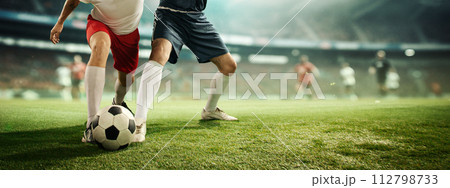 Dynamic image of male legs, football players in motion on filed dribbling ball, playing soccer at 3D stadium model with blurred background. Dynamic image of male legs, football players in motion on filed dribbling ball, playing soccer at 3D stadium model with blurred background. 112798733