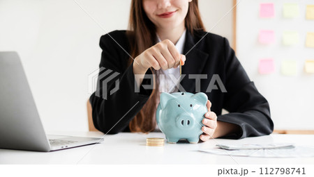 Asian woman putting coin into piggy bank. Saving money with coins Step into a business that is growing to be successful and save for retirement concepts 112798741