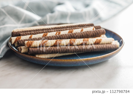 Assorted Chocolate and Vanilla Cream Filled Wafer rolls on plate on white table. Assorted Chocolate and Vanilla Cream Filled Wafer rolls on plate on white table. 112798784