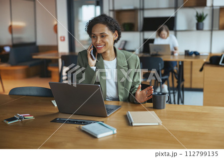 Woman at desk with laptop and cell phone on hardwood flooring in nice modern coworking office 112799135