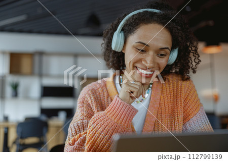 A happy woman smiles while looking at a laptop computer with audio equipment A happy woman smiles while looking at a laptop computer with audio equipment 112799139