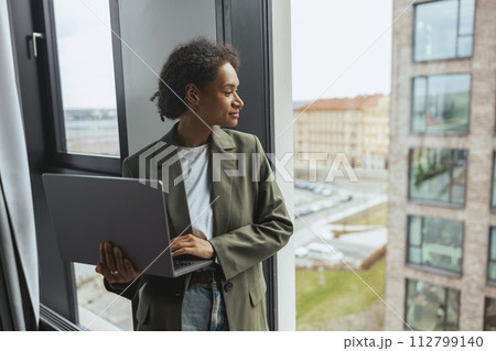 a woman is using a laptop computer while looking out of a window a woman is using a laptop computer while looking out of a window 112799140