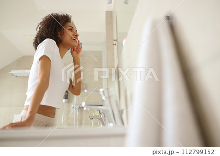 A woman is examining her face in the bathroom mirror 112799152