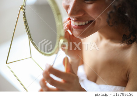 She smiles at her reflection in the mirror, showcasing her happy gesture She smiles at her reflection in the mirror, showcasing her happy gesture 112799156