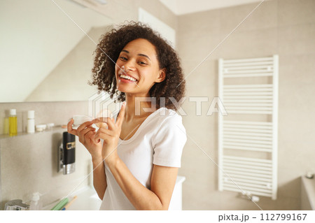 A woman smiling as she brushes her teeth in a bathroom A woman smiling as she brushes her teeth in a bathroom 112799167