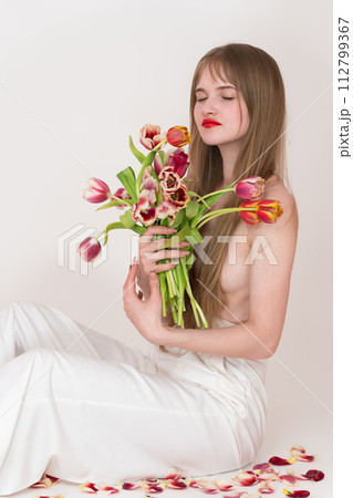 Half naked woman with closed eyes holding bouquet of tulips for Woman's Day, using them to cover her chest. Her serene expression and flowing blonde hair add to overall beauty of image 112799367