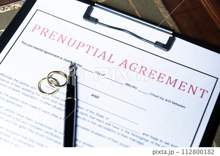 Close-up of a prenuptial agreement form with wedding rings and a fountain pen, indicating the legal aspects of marriage preparation. Close-up of a prenuptial agreement form with wedding rings and a fountain pen, indicating the legal aspects of marriage preparation. 112800182