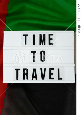 Lightbox with text TIME TO TRAVEL on background of waving UAE flag made from silk. United Arab Emirates flag with concept of tourism and traveling. Inviting greeting card, advertisement 112800572