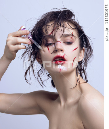 Cosmetological injections. Beautiful young woman with syringe on cheeks and scratches on face. Victim of fashion flows Cosmetological injections. Beautiful young woman with syringe on cheeks and scratches on face. Victim of fashion flows 112801978