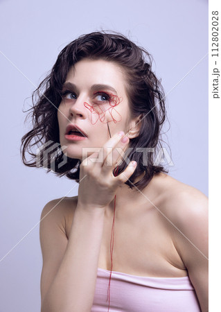 Portrait of beautiful woman with red string on face and hand with needle. Complexities of beauty, facial changes. Portrait of beautiful woman with red string on face and hand with needle. Complexities of beauty, facial changes. 112802028