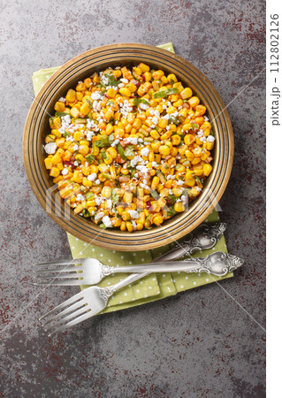 Homemade Mexican Street Corn Esquites Salad with jalapeno, cilantro, Cotija cheese, onion and spices seasoned with sour cream close-up on the plate. Vertical top view Homemade Mexican Street Corn Esquites Salad with jalapeno, cilantro, Cotija cheese, onion and spices seasoned with sour cream close-up on the plate. Vertical top view 112802126