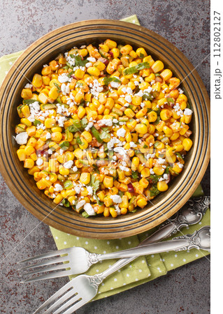 Esquites Mexican Street Corn Salad with jalapeno, cilantro, Cotija cheese, onion and spices close-up on the plate. Vertical top view Esquites Mexican Street Corn Salad with jalapeno, cilantro, Cotija cheese, onion and spices close-up on the plate. Vertical top view 112802127