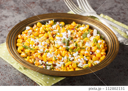 Esquites salad is a grilled Mexican corn that is slathered with a creamy sauce, seasoned with chile powder and lime juice and topped with Cotija cheese close-up on the plate. Horizontal 112802131