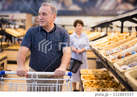 Elderly retired man buying bread and pastries in grocery section of the supermarket 112803337