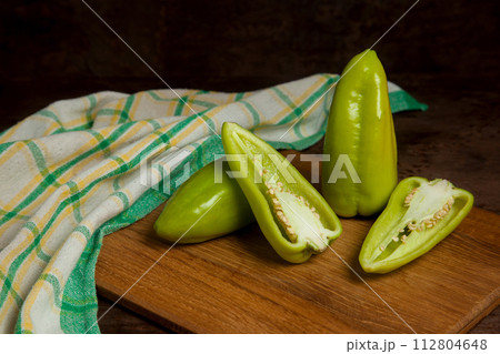 Cutting board with two whole and halves of green bell pepper and green kitchen towel on wooden background. . 112804648