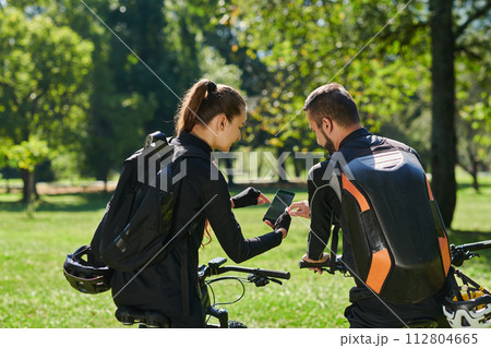 A sweet couple, equipped with bicycles and engrossed in coordinating their journey, checks their GPS mobile and watches while planning scenic routes in the park, seamlessly blending technology and A sweet couple, equipped with bicycles and engrossed in coordinating their journey, checks their GPS mobile and watches while planning scenic routes in the park, seamlessly blending technology and 112804665