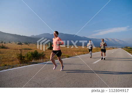 A group of friends maintains a healthy lifestyle by running outdoors on a sunny day, bonding over fitness and enjoying the energizing effects of exercise and nature 112804917