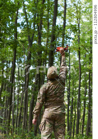 Elite military unit, equipped with state-of-the-art technology including a drone, strategically navigates and surveys dangerous wooded terrain, showcasing their precision, cooperation, and specialized Elite military unit, equipped with state-of-the-art technology including a drone, strategically navigates and surveys dangerous wooded terrain, showcasing their precision, cooperation, and specialized 112804996