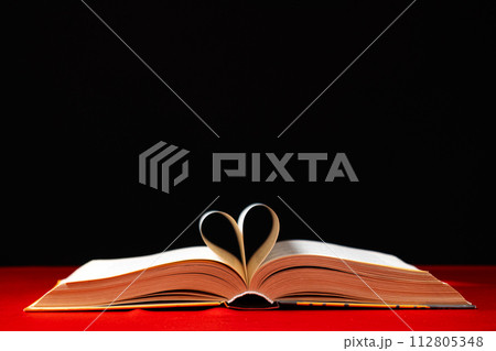 The pages of the book are folded in the shape of a heart on a red and black background, place for text The pages of the book are folded in the shape of a heart on a red and black background, place for text 112805348