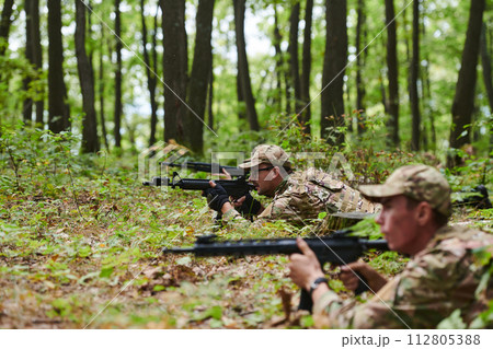 Elite soldiers stealthily maneuver through the dense forest, camouflaged in specialized gear, as they embark on a covert and strategic military mission Elite soldiers stealthily maneuver through the dense forest, camouflaged in specialized gear, as they embark on a covert and strategic military mission 112805388