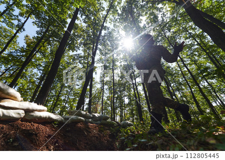 An elite soldier adeptly clears military barriers in the perilous wooded terrain, showcasing tactical skill and agility during specialized training An elite soldier adeptly clears military barriers in the perilous wooded terrain, showcasing tactical skill and agility during specialized training 112805445