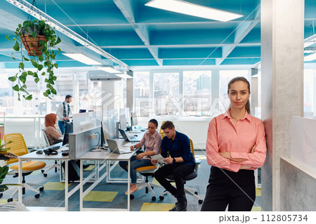 Portrait of young smiling business woman in creative open space coworking startup office. Successful businesswoman standing in office with copyspace. Coworkers working in background 112805734