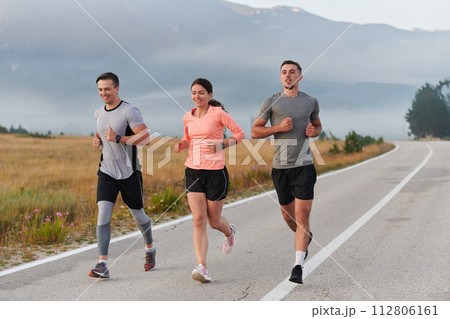 A group of friends, athletes, and joggers embrace the early morning hours as they run through the misty dawn, energized by the rising sun and surrounded by the tranquil beauty of nature A group of friends, athletes, and joggers embrace the early morning hours as they run through the misty dawn, energized by the rising sun and surrounded by the tranquil beauty of nature 112806161