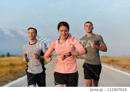 A group of friends, athletes, and joggers embrace the early morning hours as they run through the misty dawn, energized by the rising sun and surrounded by the tranquil beauty of nature A group of friends, athletes, and joggers embrace the early morning hours as they run through the misty dawn, energized by the rising sun and surrounded by the tranquil beauty of nature 112807628